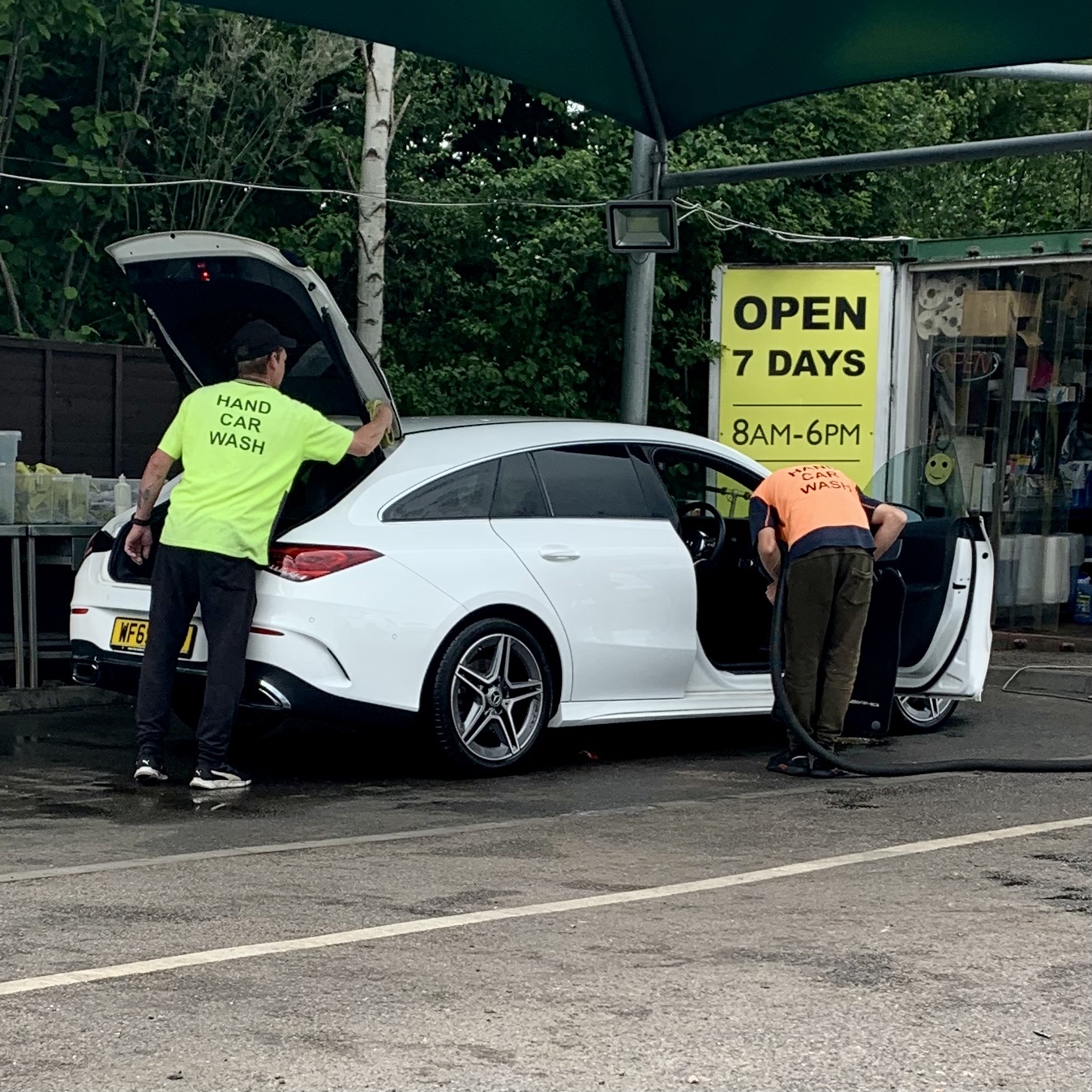 Two members of the Elite Valeting team, in branded hand car wash shirts, cleaning a customer's car